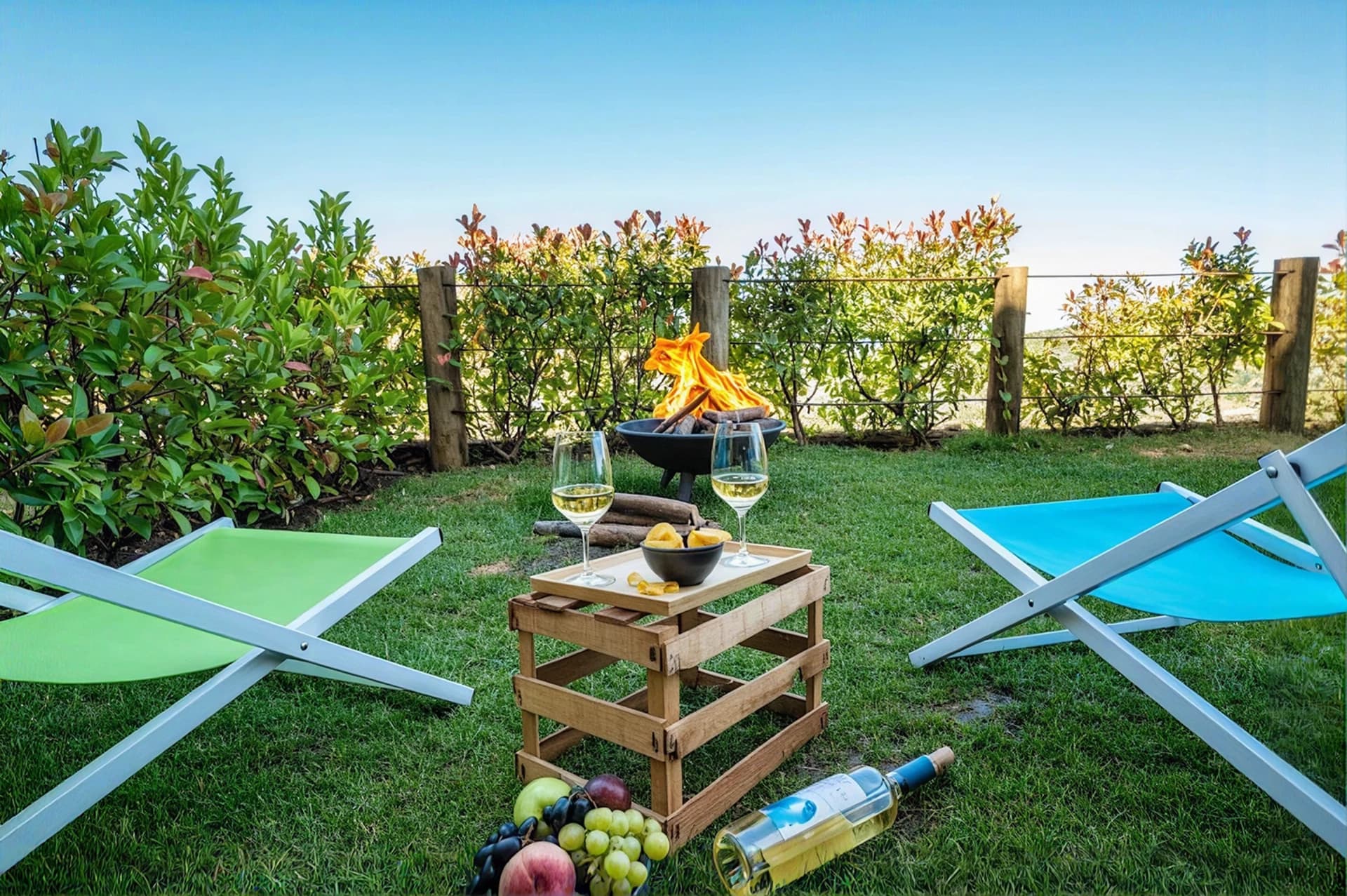 Lounge chairs around a lit fire pit with wine and fruit